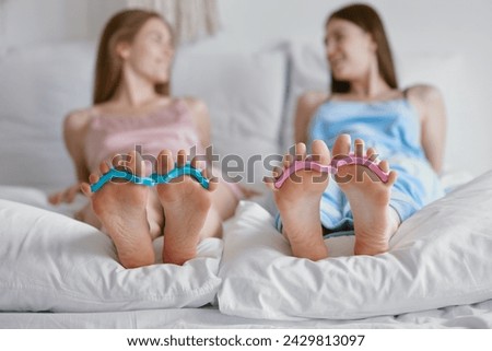 Closeup feet with toe spacers of young woman friends lying in bed Royalty-Free Stock Photo #2429813097