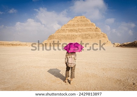 View of a woman with a purple umbrella watching the scale pyramid of Djoser in the Saqqara necropolis. Royalty-Free Stock Photo #2429813897