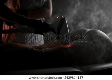 Cosmetologist's female hand runs over a woman's leg, on which a special gel with a photoepilator with a red glow has been applied Royalty-Free Stock Photo #2429814137