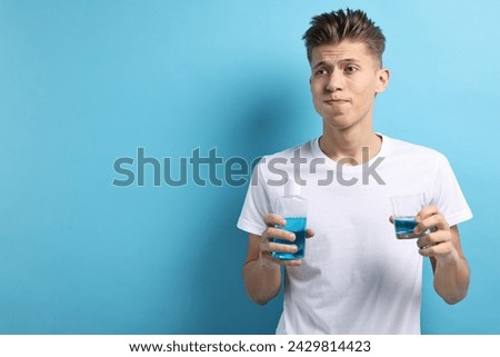 Young man using mouthwash on light blue background, space for text Royalty-Free Stock Photo #2429814423