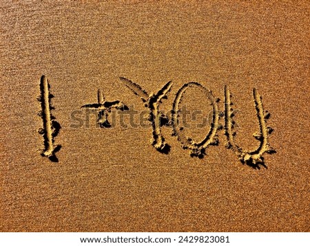 The image displays ‘I + YOU’ deeply etched into a sandy surface.