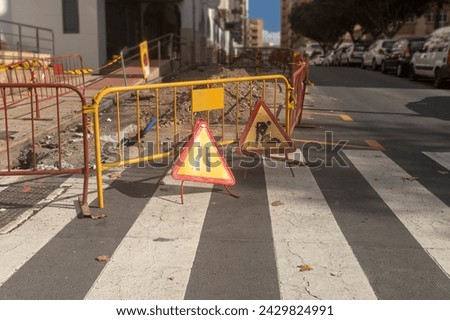 This photo depicts a collection of signs and barricades announcing a construction zone on a city street during daylight hours. The signage and safety barriers to alert pedestrians and drivers