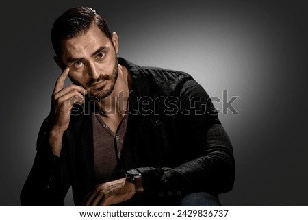 Handsome brutal macho guy posing on dark gray background, Young man's intense demeanor captured in a powerful, dark-themed portrait Royalty-Free Stock Photo #2429836737