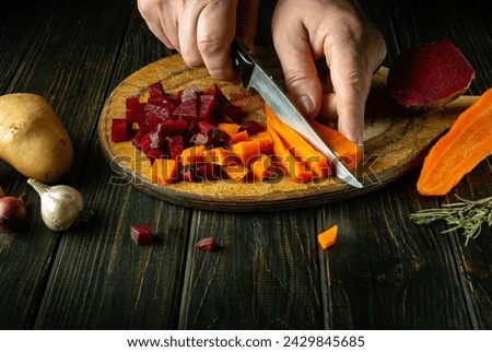 Close-up of a man's hands using a knife to cut boiled vegetables on a kitchen cutting board. The concept of cooking venegret or Ukrainian national dish.