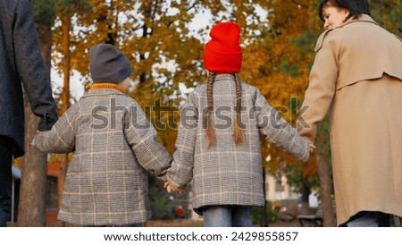 Parents clasp hands with children among trees in park in autumn. Son and daughter keep parents hands crossing autumn park. Pleased boy and girl enjoy time together with parents during autumn holiday