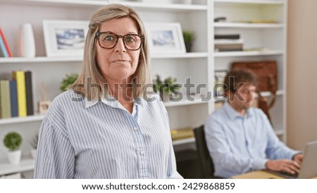 Two workers, a man and woman, face the harsh reality of work, serious countenances stuck to their faces while toiling away at the office, fully immersed in the world of gadgets and tech. Royalty-Free Stock Photo #2429868859