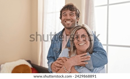 Confident mother and son share a warm, smiling hug indoors, enjoying their love-filled, casual lifestyle in their happy home. Royalty-Free Stock Photo #2429868891