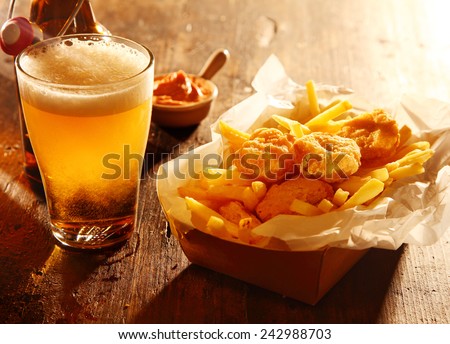 Chilled glass of draft beer served with fried battered fish and French fries accompanied by a savory dip in a bar, tavern or pub Royalty-Free Stock Photo #242988703