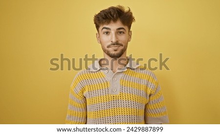 Stylish young arab man coolly bears his serious expression, standing lone against a stark yellow background. Royalty-Free Stock Photo #2429887899