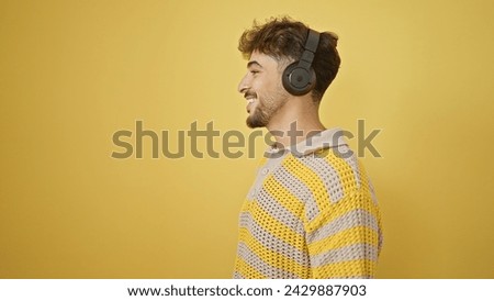 Smiling young arab man coolly enjoying music, listening with headphones on, exuding confidence over an isolated yellow background Royalty-Free Stock Photo #2429887903