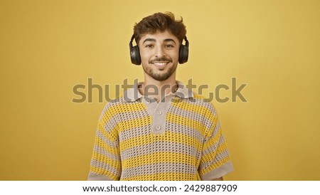 Smiling young arab man coolly enjoying music, listening with headphones on, exuding confidence over an isolated yellow background Royalty-Free Stock Photo #2429887909
