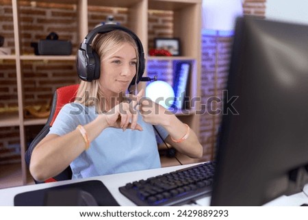 Young caucasian woman playing video games wearing headphones rejection expression crossing fingers doing negative sign 