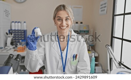 A cheerful young woman in a lab coat holding a medicine bottle in a bright laboratory setting. Royalty-Free Stock Photo #2429891609