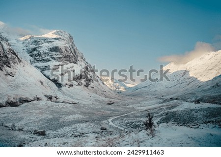 A path winds through a snow-covered landscape with the Three Sisters mountains rising up on the left. Glencoe, Scottish Highlands 
