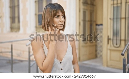 Stunning young hispanic woman holding a serious, focused, conversation on her smartphone while standing coolly on a sun-soaked city street. Royalty-Free Stock Photo #2429914667