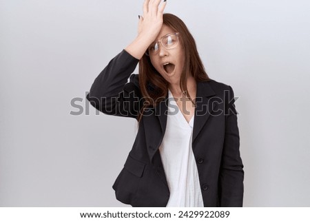 Beautiful brunette woman wearing business jacket and glasses surprised with hand on head for mistake, remember error. forgot, bad memory concept.  Royalty-Free Stock Photo #2429922089