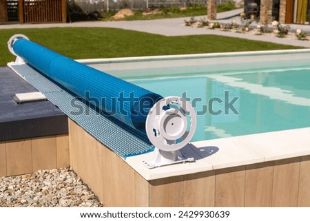 Swimming pool cover for protection against dirt, leaves, heating and cooling water, copy space. Blue tarpaulin pool cover. Summer day Royalty-Free Stock Photo #2429930639
