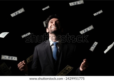 An elated businessman in a dark suit surrounded by flying cash, representing financial success or windfall.


