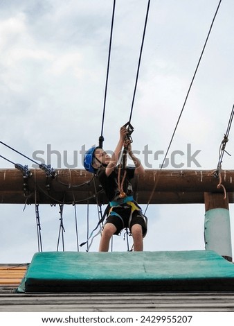 A teenage boy descends on a rope suspension bridge in a rope amusement park. Active youth sports recreation