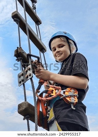 A teenage boy climbs a rope ladder in a rope amusement park and smiles. View from below. Active youth sports recreation