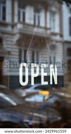 Inviting Open Sign in Glass Window, Welcome Message for Customers. Transparent sign with bold letters reflects the bustling city life