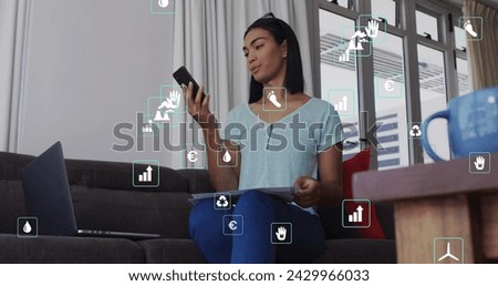 Image of ecology icons over biracial woman using smartphone. Global business, finances and digital interface concept digitally generated image.