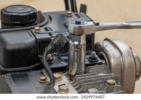 Removing spark plug from lawn mower engine with socket wrench. Lawn and garden equipment repair, maintenance and service. Royalty-Free Stock Photo #2429974407