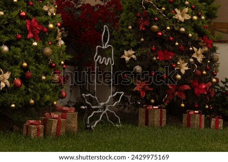 One LED lights candle Christmas decoration surrounded by golden and red gifts under trees with festive ornaments