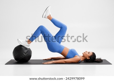 Fitness woman doing glute bridge exercise with med ball on gray background. Athletic girl working out