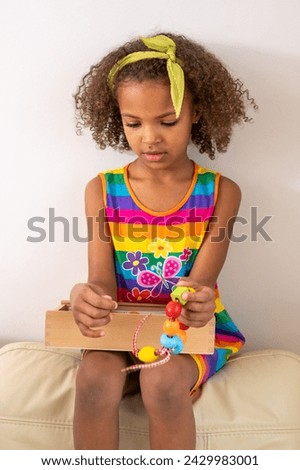 Focused mixed race girl threading beads, wearing a colorful dress with a green headband. Captures concentration and dexterity in creative play and development trough toys. High quality photo