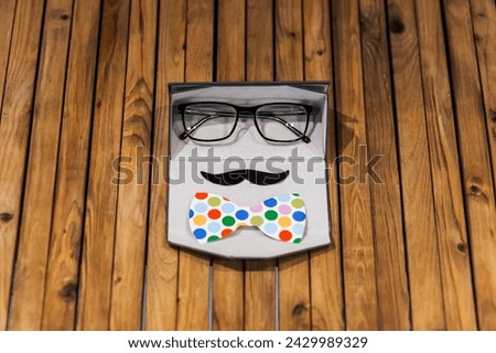 Photo props of glasses, paper mustache, colored bow tie in a case on a wooden background for a carnival. Photo of a gentleman's face, concept, copy space.