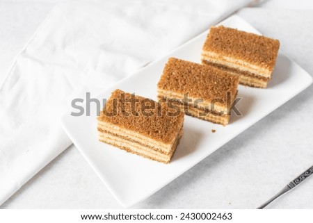slice of vanilla cake with jam filling, thin layers of vanilla and chocolate cake with jam filling on a white background Royalty-Free Stock Photo #2430002463
