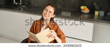 Close up portrait of beautiful young woman holding notebook, reading planner, sitting at home and studying, revising or doing homework.