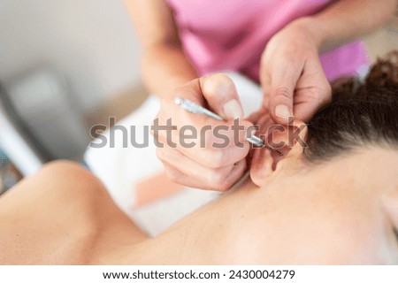 Crop masseuse applying flexible massage ear pen during auriculotherapy tr in salon Royalty-Free Stock Photo #2430004279