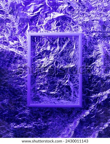 White  empty photo frame on aluminum foil lit by graduated neon blue light. Abstract colorful background. Space for design.