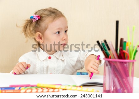 Cute child girl drawing with colorful pencils and felt-tip pen in preschool at table in kindergarten