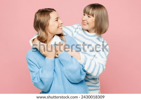 Elder happy parent mom 50s years old with young adult daughter two women together wear blue casual clothes hug embrace look to each to each other isolated on plain pink background. Family day concept