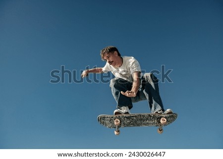 Active man doing tricks in the air on his skateboard at the skate park on blue sky background