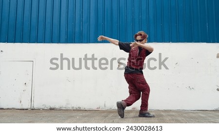 Handsome street dancer practicing break dancing at white back ground. Sport man wearing hip hop style while moving footsteps to music at street with blue background. Outdoor sport 2024. Endeavor.