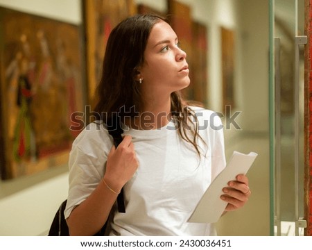 Focused girl visiting an exhibition in a museum looks with interest at the exhibit located behind the glass Royalty-Free Stock Photo #2430036451