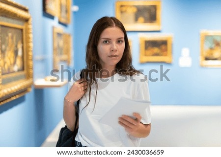 Portrait of a focused interested girl visitor with an information booklet in hand in an paintings gallery Royalty-Free Stock Photo #2430036659