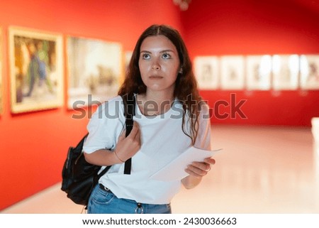 Portrait of a young girl visitor with a paper guide at the exhibition of paintings in the museum Royalty-Free Stock Photo #2430036663