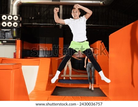 Joyful young man captured in mid-air while jumping on trampolines against backdrop of vivid colorful setting of indoor amusement park.. Royalty-Free Stock Photo #2430036757