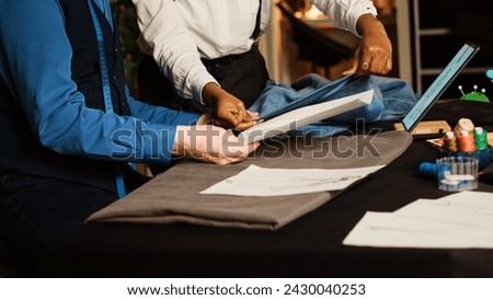 Old craftsman and trainee working in atelier, checking sketches of clothes to manufacture fashion design. Beginner learning the art of handcraft from experienced tailor. Handheld shot.