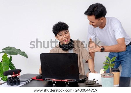 Two young Asian freelance video editors working together, with one showing an editing technique to his friend.