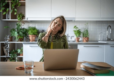Frustrated woman with closed eyes suffering from pain, discomfort caused by sitting at uncomfortable work place while working freelance at home, massaging neck, stretching to release muscle tension Royalty-Free Stock Photo #2430062443