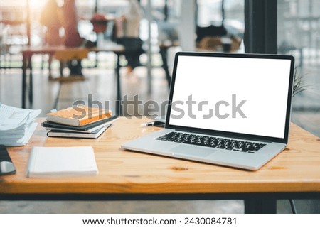 An organized work setup featuring a laptop with a blank screen, notebooks, and a plant on a wooden table in a bright office.