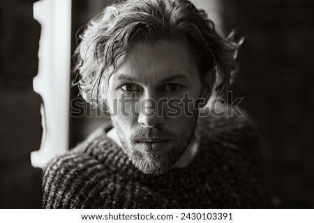 Art black and white portrait of an adult mature man with curly hair, wearing a loose knitted sweater, looking intently at the camera. People, emotions. Psychological picture.
