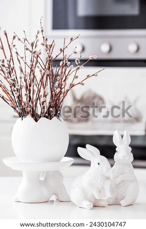 A bouquet of willow twigs for the Orthodox Palm Sunday holiday. Willow in a white egg and Easter bunnies in the interior of a modern white kitchen. Royalty-Free Stock Photo #2430104747