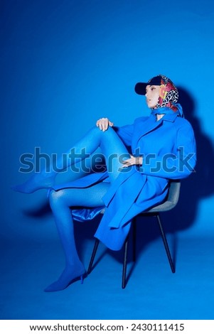 fashion portrait of young elegant woman in blue coat. Total blue monochromatic fashion look, blue tights, blue background